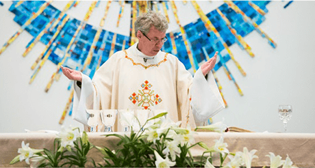 Father Urrabazo, in white habit with arms raised, blessing communion cups on top of altar.